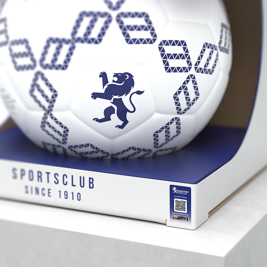 一个印有蓝色几何图案和狮子徽章的白色足球,包装上印有“Sportsclub Since 1910”字样。足球采用激光光刻VeoMark®技术,集公开和隐蔽防伪功能于一体,可有效防止假冒。该解决方案可确保产品真实性,提升品牌信任度。